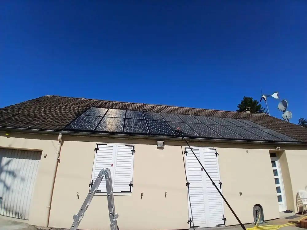 Toiture photovoltaïque en cours de nettoyage à la perche : les modules déjà traités renvoient la lumière, les autres restent ternes